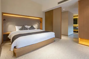 A minimalist bedroom featuring a wooden platform bed, concrete floor, and fabric headboard with embedded lighting.