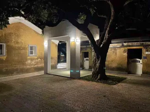 A minimalist entryway with a wooden façade and white walls, illuminated by warm lighting under a large tree at night.