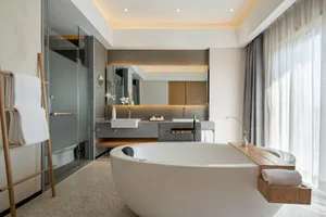 A modern minimalist white bathroom with a large freestanding tub, a double sink vanity, and a glass-enclosed shower.