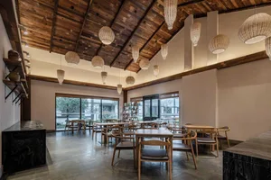 A modern cafe interior with wooden tables and chairs, a high wooden ceiling, and wicker pendant lights.