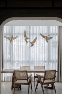 Modern dining room with wooden table and chairs, adorned with wooden bird sculptures hanging from the ceiling, set against sh