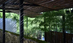 A modern garden featuring a bamboo shade structure with a natural stone wall and greenery.