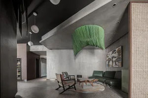 A modern lounge area featuring concrete walls and ceiling, industrial pendant lights, and green decorative elements.
