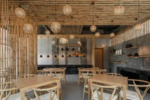 A modern restaurant interior featuring natural wood tables, chairs, and ceiling with hanging light fixtures.