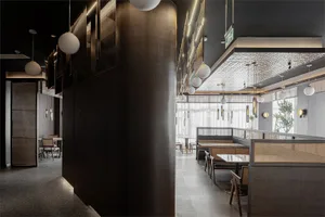 Modern restaurant interior with wooden furnishings, metallic accents, glass walls, and fabric banquettes.