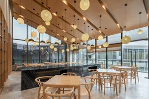 A modern restaurant interior featuring wooden tables and chairs, stone accents, and hanging glass light fixtures.