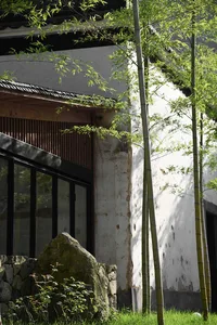 A stone and bamboo exterior of a building with tall green bamboo trees beside it.