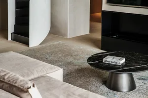 A modern living room featuring a marble coffee table with an Alvar Aalto book on it, a light-colored sectional sofa, and a sl