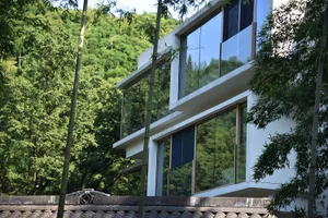 一座現代簡約住宅建築，擁有玻璃牆面、混凝土結構、白色牆面，以及周圍的竹林景觀