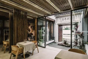 A modern restaurant interior with an indoor garden featuring a wooden table and chairs, glass walls, and concrete flooring.