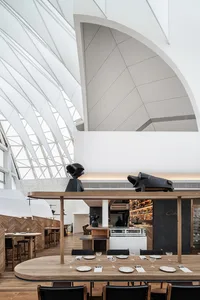 Modern restaurant interior with white walls, wood tables, concrete floor, and metal accents.