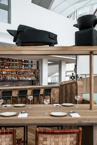 Modern restaurant interior with wooden tables, metal stools, and glass shelves displaying liquor.