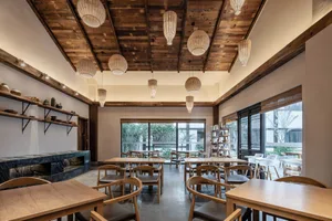 A modern restaurant interior featuring wooden beams on the ceiling and wooden tables and chairs.