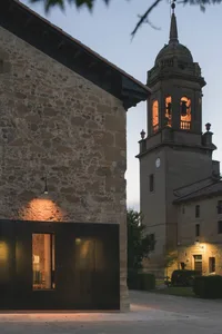 A historical church building made of stone with a illuminated bell tower at dusk.