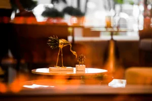 A golden flamingo sculpture with a small pinecone on the floor.