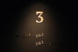 Gold metallic hotel room numbers on dark wall for floor 3.