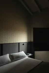 Minimalist bedroom with white bedding and black accents, textured brown brick wall