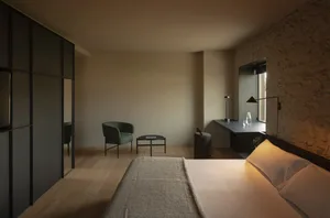 A minimalist bedroom with wooden floors, stone walls, and simple furnishings.