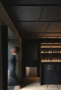 A minimalist wine bar with concrete walls, a black bar top, and warm lighting.