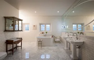 A modern bathroom with white tiles, marble floors, and a large white bathtub.
