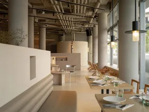 Modern restaurant interior with minimalist design, concrete and steel materials, and an open, airy atmosphere.