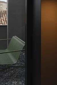 A modern metal bench with curved lines outdoors near a black wall.