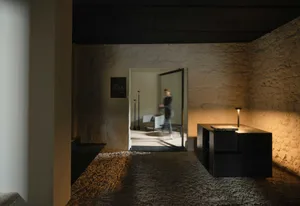 A minimalist hotel lobby with a modern design featuring concrete walls and floors, and sleek furniture.