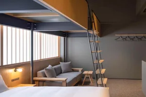 Modern minimalist bedroom with a loft bed, grey sofa, and wooden materials.