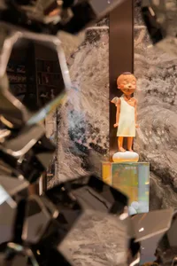 A modern marble sculpture displayed on a glass pedestal in a room with marble walls.