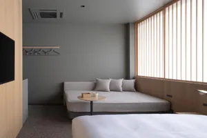 A minimalist bedroom with a white bed, a light gray couch, and a small table.
