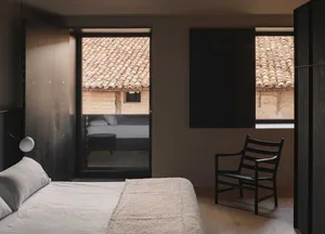 Modern minimalist bedroom featuring concrete walls, a bed with white sheets, and a chair.