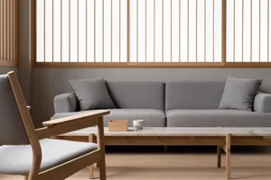 A modern minimalist living room with a grey sofa, wooden armchair, and marble coffee table.