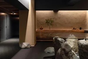 現代餐廳室內空間，混凝土牆面點綴岩石元素，搭配玻璃餐桌與自然岩石及花瓶