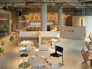 Modern minimalist restaurant interior with concrete pillars, wood benches, and round tables.