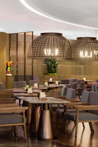 A modern restaurant interior with metal pendant lights, wooden tables, and glass panels.