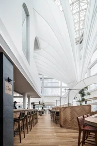 Modern restaurant interior with wooden tables, metal stools, and glass windows.