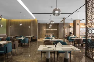 Modern restaurant interior with white marble tables and chairs, pendant lights, and green accents.