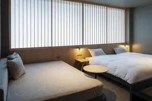 A modern minimalist bedroom featuring soft furnishings and a large window with light filtering shades.