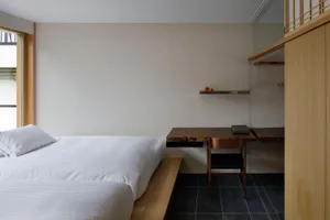 A minimalist bedroom with two beds, a wooden desk, and a floating shelf.