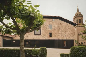 The exterior of a modern building made of stone with large windows and a tree in the foreground.