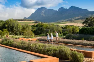 Three people walking along a path in a modern landscape garden with metal arches and water features.