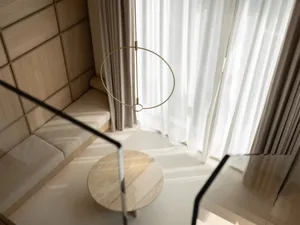 A minimalist interior design featuring a circular brass pendant light and white curtains.