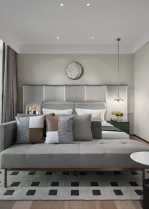 A minimalist bedroom featuring a grey fabric bed with multiple cushions, a green nightstand, and a round ceiling light.