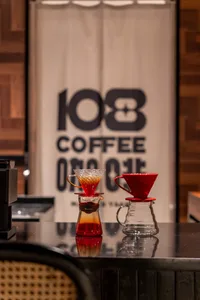 A photo of two coffee brewing tools on a counter inside a coffee shop, with a banner in the background.