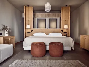 A minimalist bedroom with a wooden bed frame, white bedding, and two brown poufs.