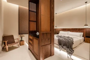A minimalist bedroom featuring white walls and a wooden bed frame with a grey blanket draped over it.