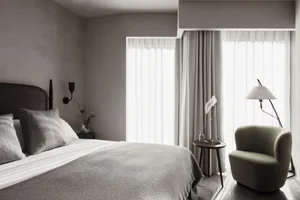 A minimalist bedroom with a bed, white curtains, and a green armchair.