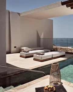 Modern minimalist patio area with concrete floor, stone walls, and wood furniture featuring a lounge area with white cushions