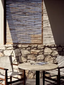 A minimalist patio with stone and wooden furniture under a bamboo shade.