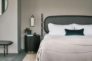 A modern bedroom featuring a fabric bed with a black headboard on a grey floor, accompanied by a side table with a lamp and a